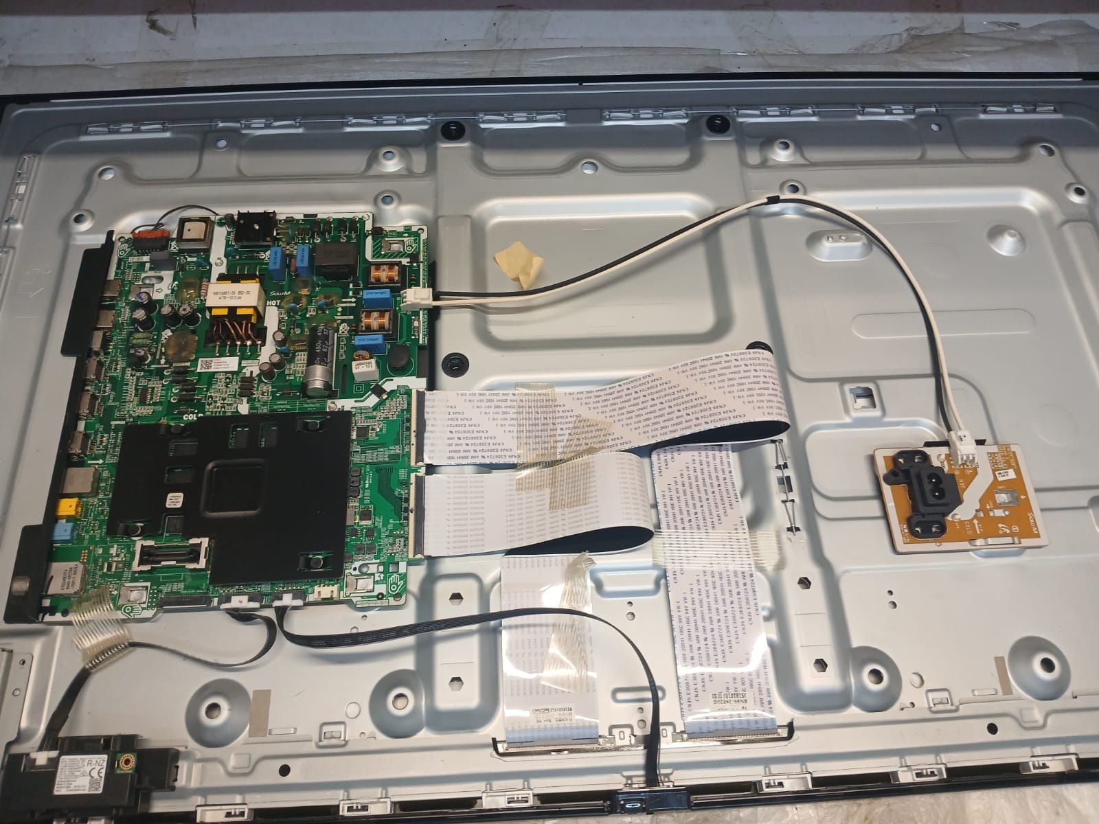 Televizor Samsung deschis pe banc: sursa, placa de bază și cablurile panglică spre panou